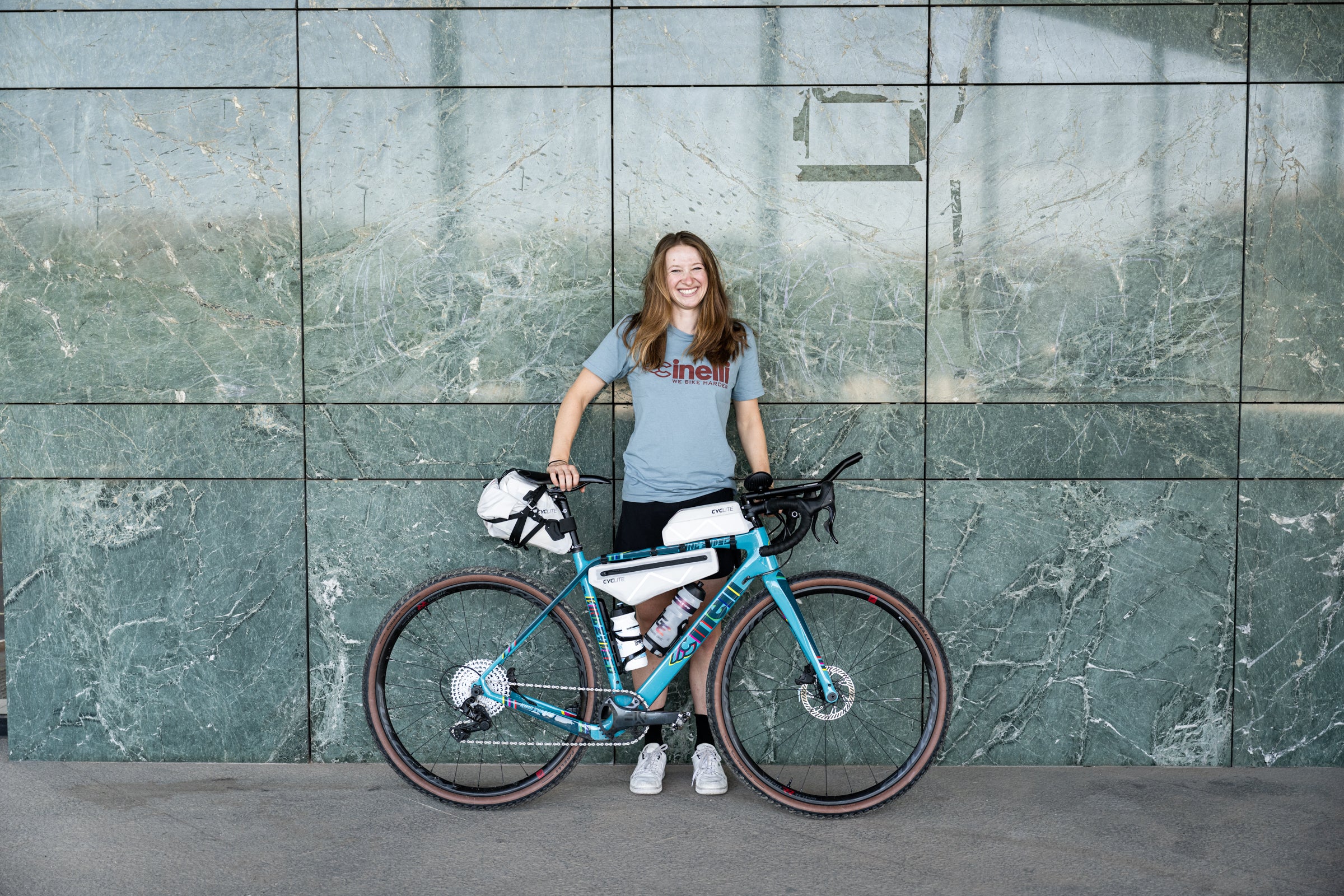 Luisa, standing behind her packed bike against a blue wall.